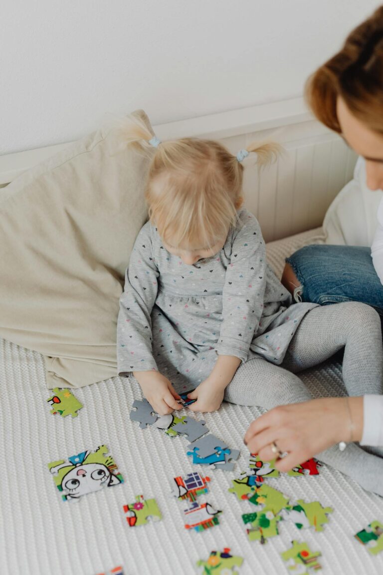 A young blonde child solving a colorful puzzle indoors with an adult. Bright and playful scene.